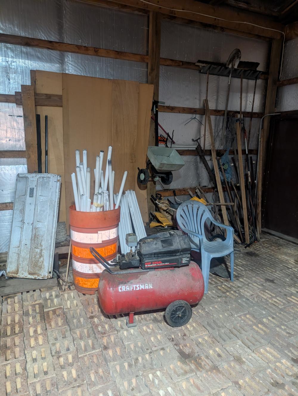 garage side wall items - light bulbs, barrel, spreader, push brooms, air compressor (works but has a hole in the tank), shovel, tree trimmer, barb wire, misc tools