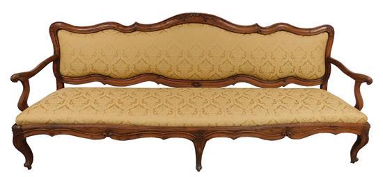 Italian sofa, 18th C., walnut, shaped frame with carved foliate crest and knees, upholstered back and seat in golden wheat colored d...