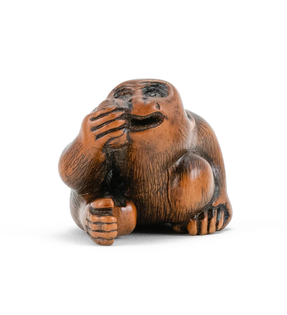WOOD NETSUKE In the form of a monkey with inlaid eyes eating a piece of fruit. Length 1.75".