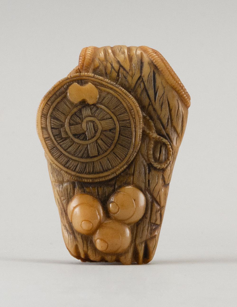 CARVED BONE NETSUKE In the form of three pearls and a straw hat lay on a rain cape. Length 2.5".