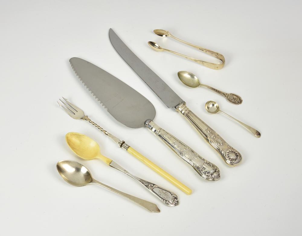 A small collection of silver and white metal cutlery comprising a bone handled pickle fork; a silver mounted bone teaspoon; a dognos...