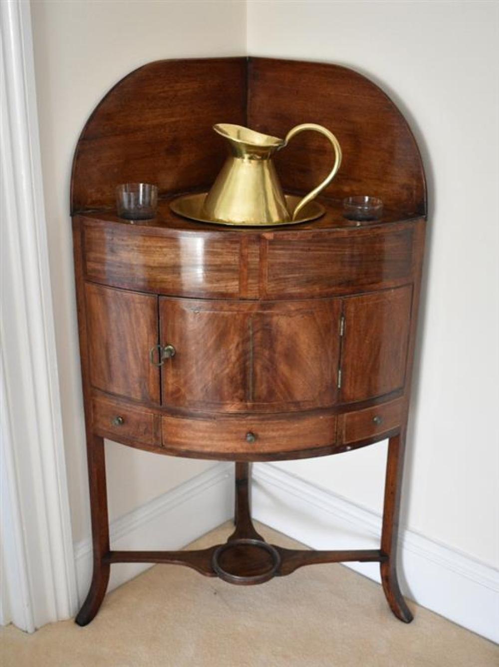A George III mahogany corner washstand the arched back over a top with later brass jug and bowl,