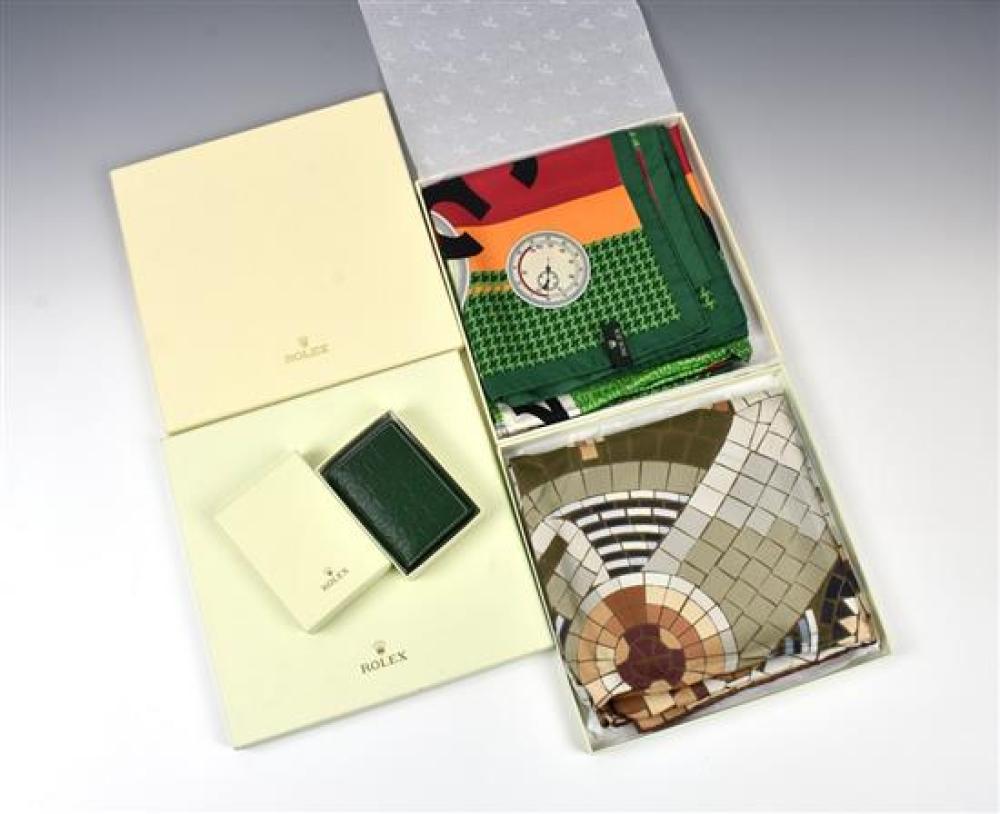 Two Rolex ladies silk scarves in the original lidded boxes; together with a boxed Rolex dark green embossed leather wallet. (3)