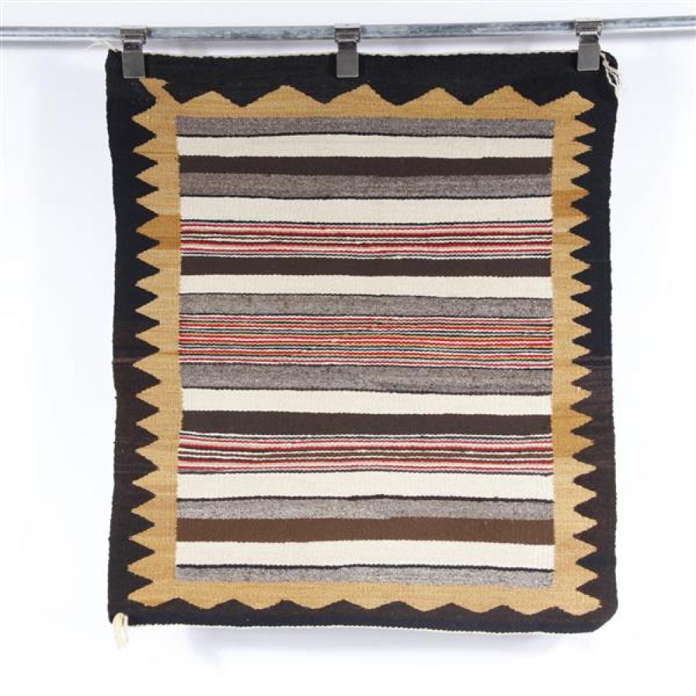 Navajo saddle blanket weaving with black and gold zig zag border and multicolored stripes in shades of brown, ream and red.